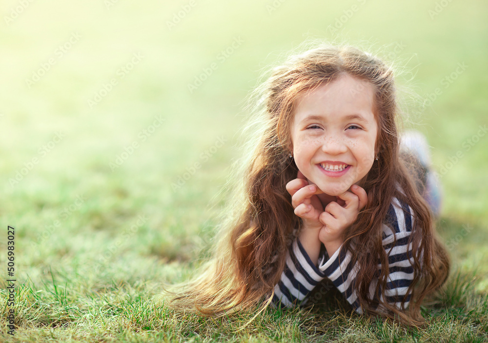 Naklejka premium a little girl with long fluffy hair is now lying on the grass and laughing looking at the camera