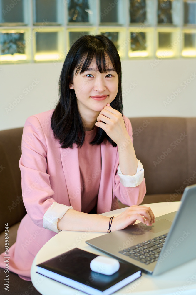 Portrait of Asian young girl looking at camera while sitting at table of cafe with laptop Portrait of Asian young girl looking at camera while sitting at table of cafe with laptop