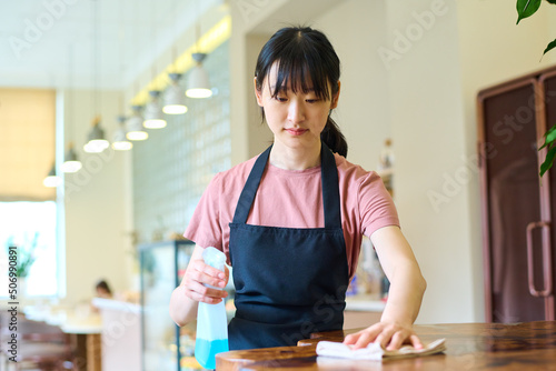 Female restaurant employee wiping the dining table in preparation to welcome customers