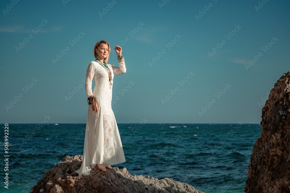 Woman in bohemian clothing on beach at sunset. Boho style for fashionable look on resort. Middle aged well looking woman in white dress and boho style braclets. Summer fashion Stock Photo