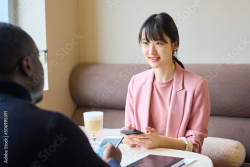 Asian young businesswoman using her mobile phone and consulting man during their meeting at cafe photo