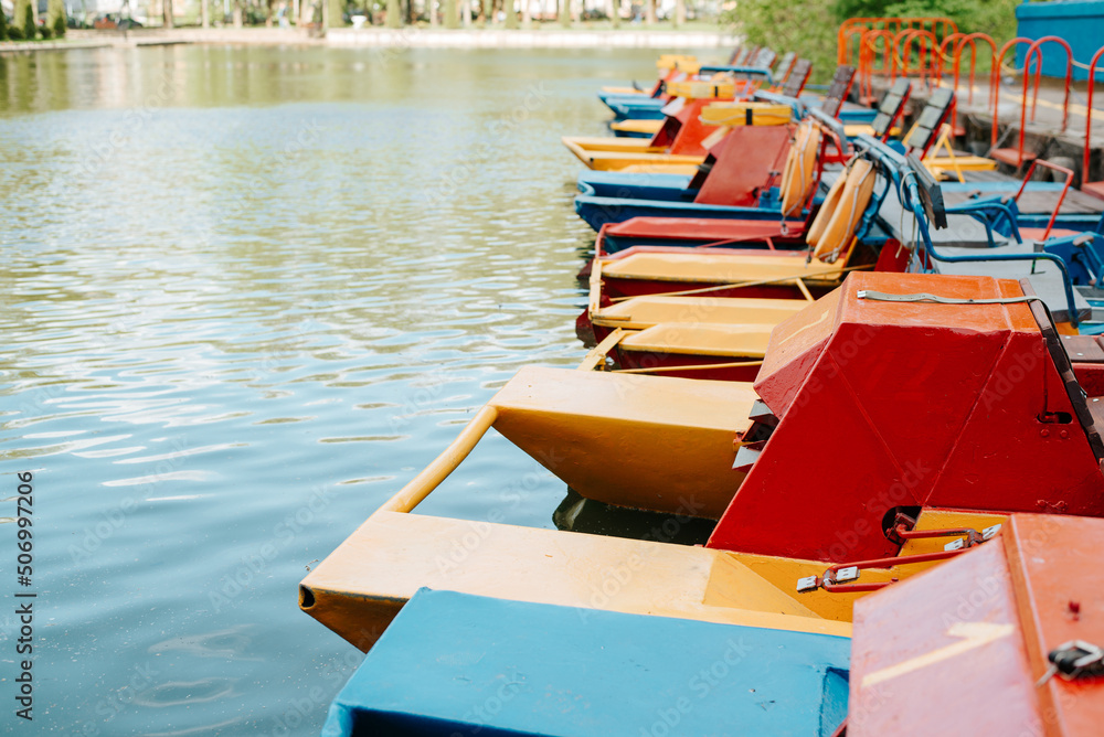 Obraz premium Boat station of catamarans in park on sunny day. Side view of parked multicolored catamarans on water. Selective focus, copy space