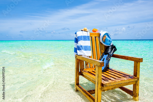 A wooden chair in the Indian Ocean with a towel, shell, flippers and inderwater mask. photo