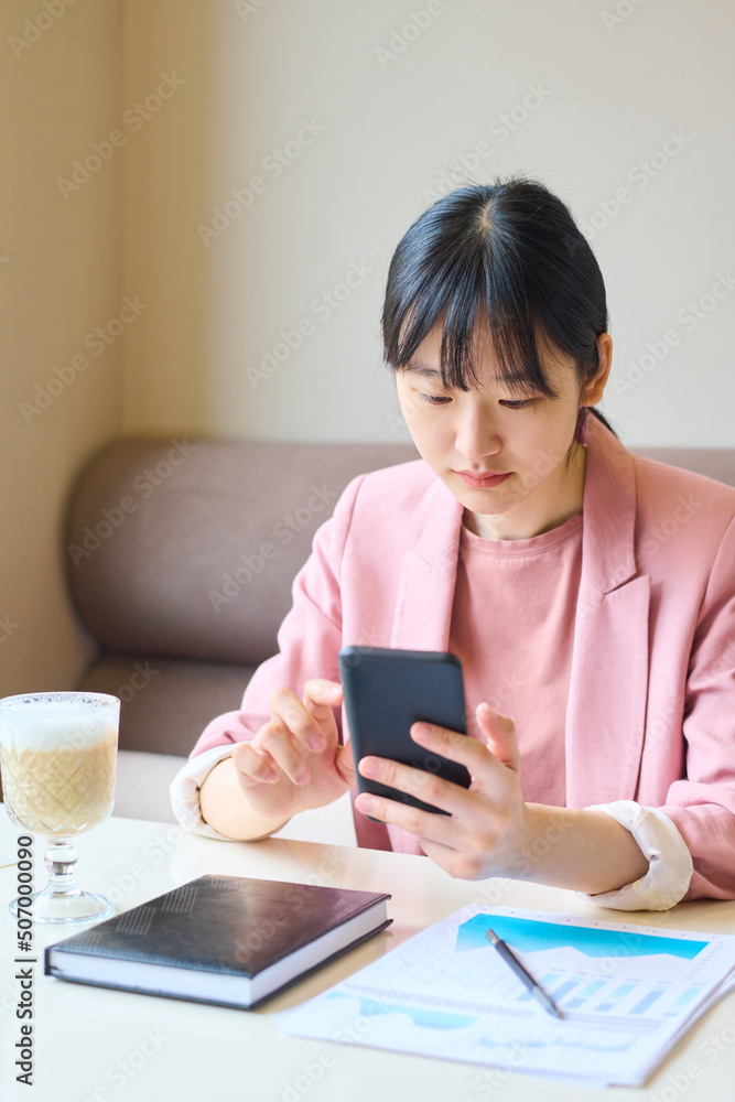 Asian young businesswoman using her mobile phone while drinking coffee at table at restaurant Asian young businesswoman using her mobile phone while drinking coffee at table at restaurant
