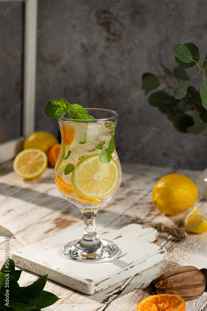 Fototapeta premium Ice-cold non-alcoholic lemon cocktail decorated with a sprig of mint on a light wooden background. Close-up