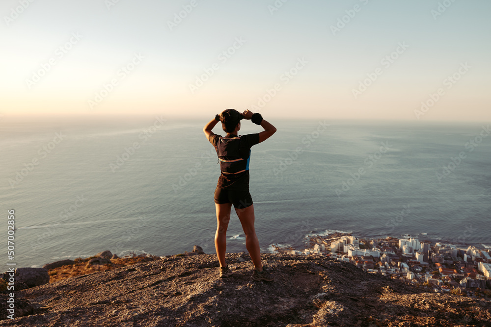 Back view of runner standing on the edge and enjoying the view at sunset