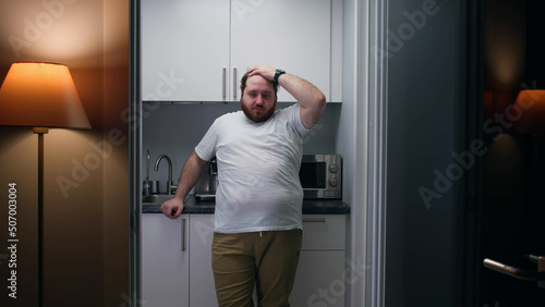Portrait of frustrated overweight man stand in small kitchen