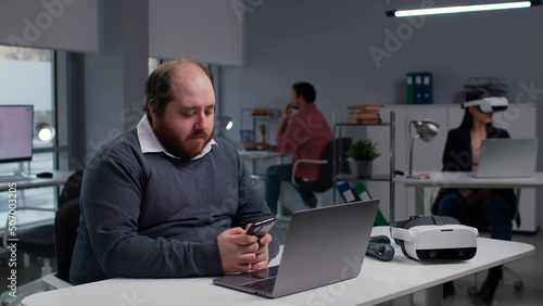 Overweight manager using smartphone sitting at desk in modern office