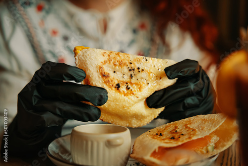 Delicious lunch in restaurant. Woman hands in black gloves are holding traditional pitas sandwich. Dish of corn bread with fish and salad inside. Cafe menu.