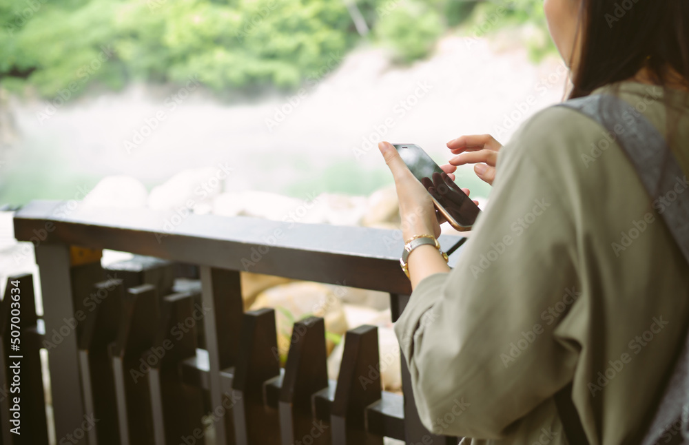 Cropped close up of portrait woman wearing casual clothes holding smartphone, looking at its screen while standing in park. Holiday activity, vacation, lifestyle and technology concept.