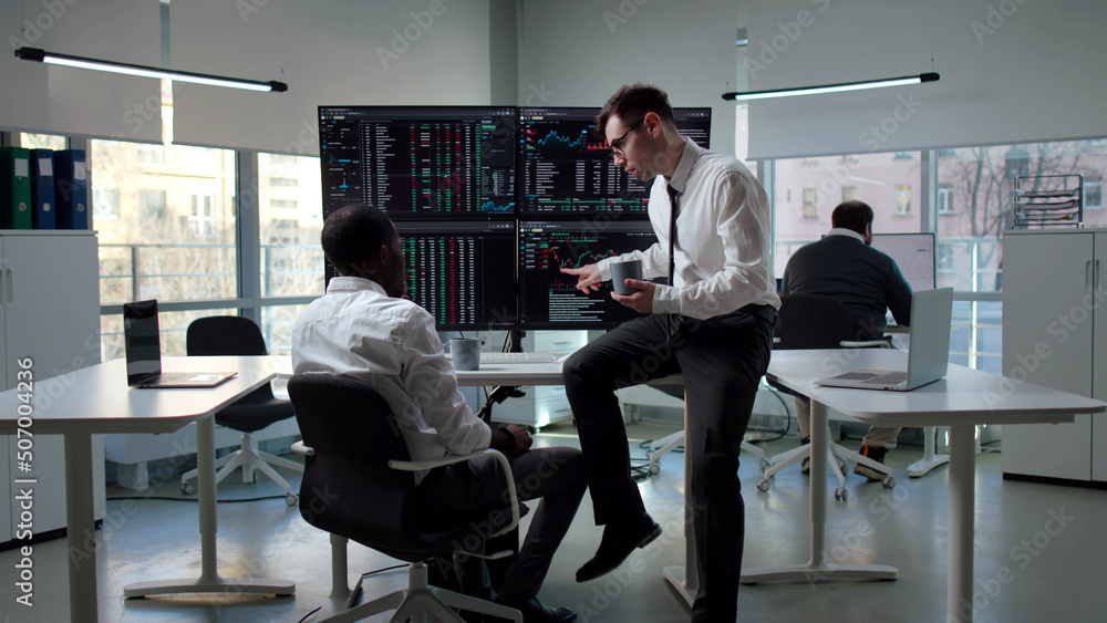 Two brokers monitoring financial graphs and drinking coffee