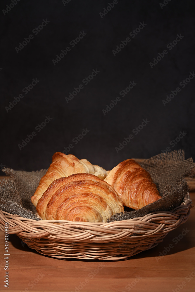 Fresh croissants in a basket on a wooden table for homemade breakfast