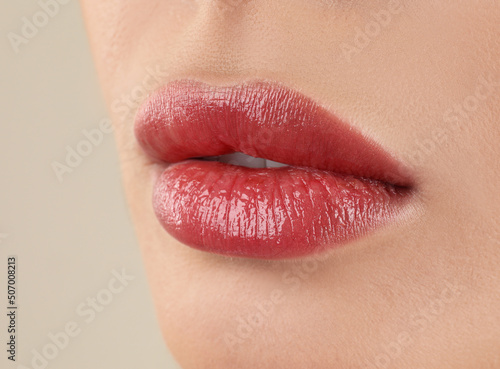 Woman with beautiful perfect lips after permanent makeup procedure on beige background, closeup