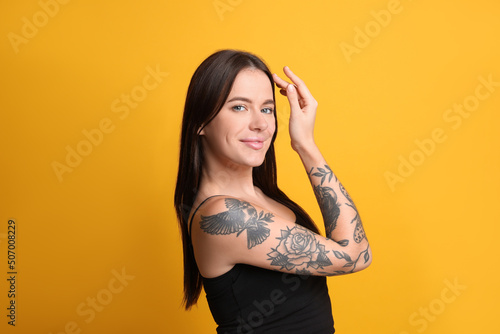 Beautiful woman with tattoos on arm against yellow background