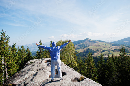 Happy hiker with hands in the air stand on rock. View over rocky valley.