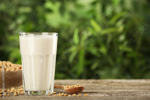 Glass with fresh soy milk and grains on white wooden table against blurred background. Space for text