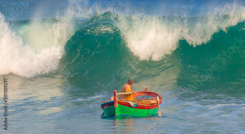 Fototapeta Naklejka Na Ścianę i Meble -  A fisherman goes out to sea to catch fish, in the background a very strong sea wave is coming towards him