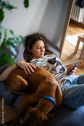 Portrait of a young woman with a Hungarian Pointer dog and a small kitten in her arms lying at home in a room on a bag chair