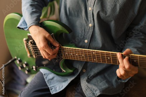 Photography Close-up of a musician playing a green electric guitar and wearing denim clothes