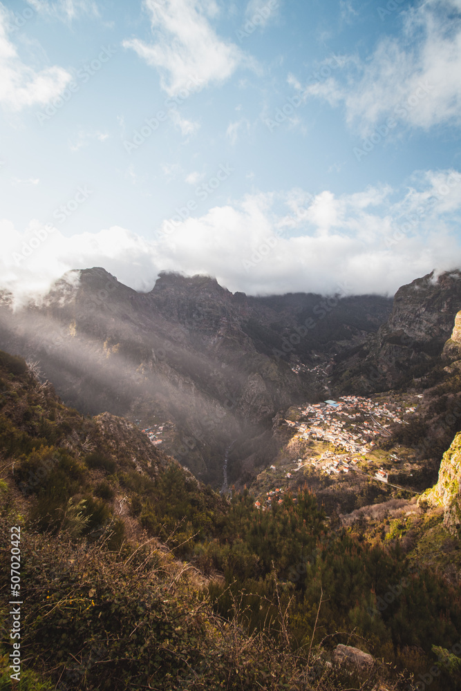 Fototapeta premium Very well-known tourist destination, Curral das freiras, a village nestled in the mountains with minimal sunlight. Aerial view of valley of nuns at sunset and peak of mountains in fog