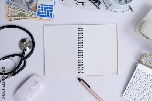 Blank notepad with a pen rests on an office desk table, surrounded by computer equipment and various papers. flat lay, top view, money and banking background