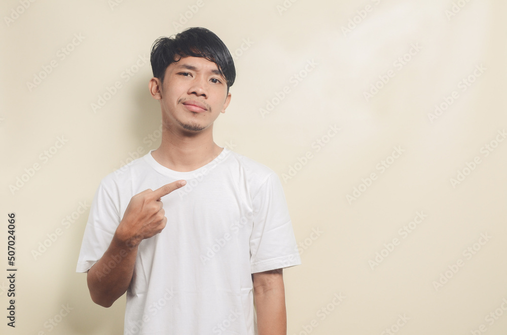 asian man wearing white t-shirt pointing to empty space on isolated background asian man wearing white t-shirt pointing to empty space on isolated background