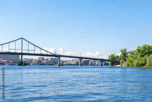 Scenic nature travel cityscape river Dnipro with blue water and metal pedestrian bridge at sunny summer day in Kiev. View from inside river, ship on water