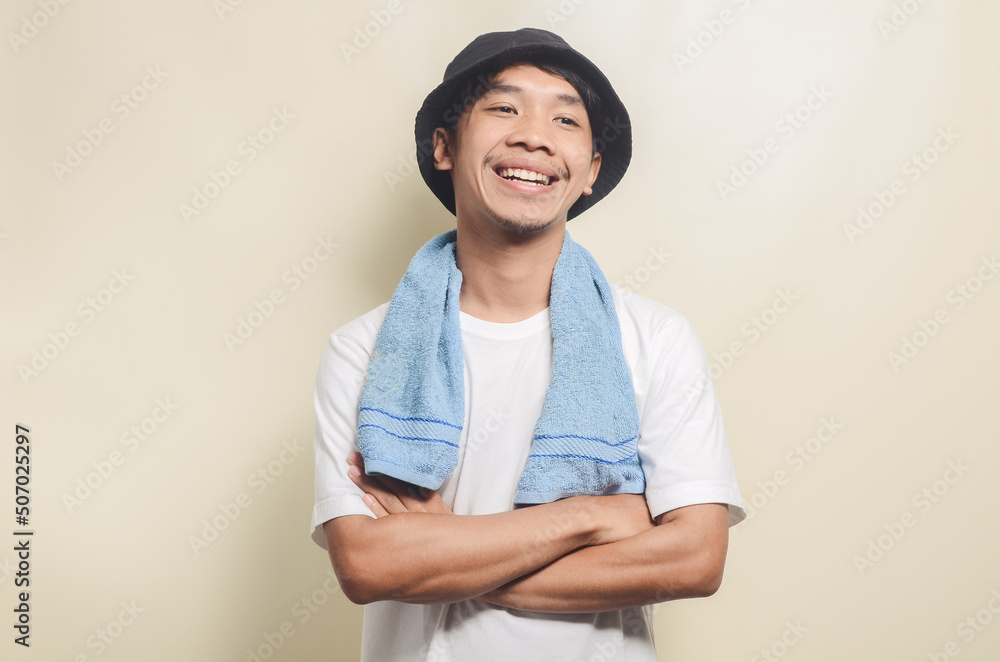 happy asian man wearing bright white t-shirt with black hat carrying blue towel on isolated background happy asian man wearing bright white t-shirt with black hat carrying blue towel on isolated background
