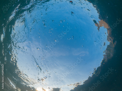 View of the blue sky through the thickness of the turquoise sea water. Underwater photo. Bottom up view