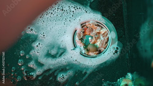 The person is busy with household chores and collects leftover food from dirty dishes in a strainer filter to prevent clogging the sewer and drainage system. Routine. Water flows from tap into sink. photo