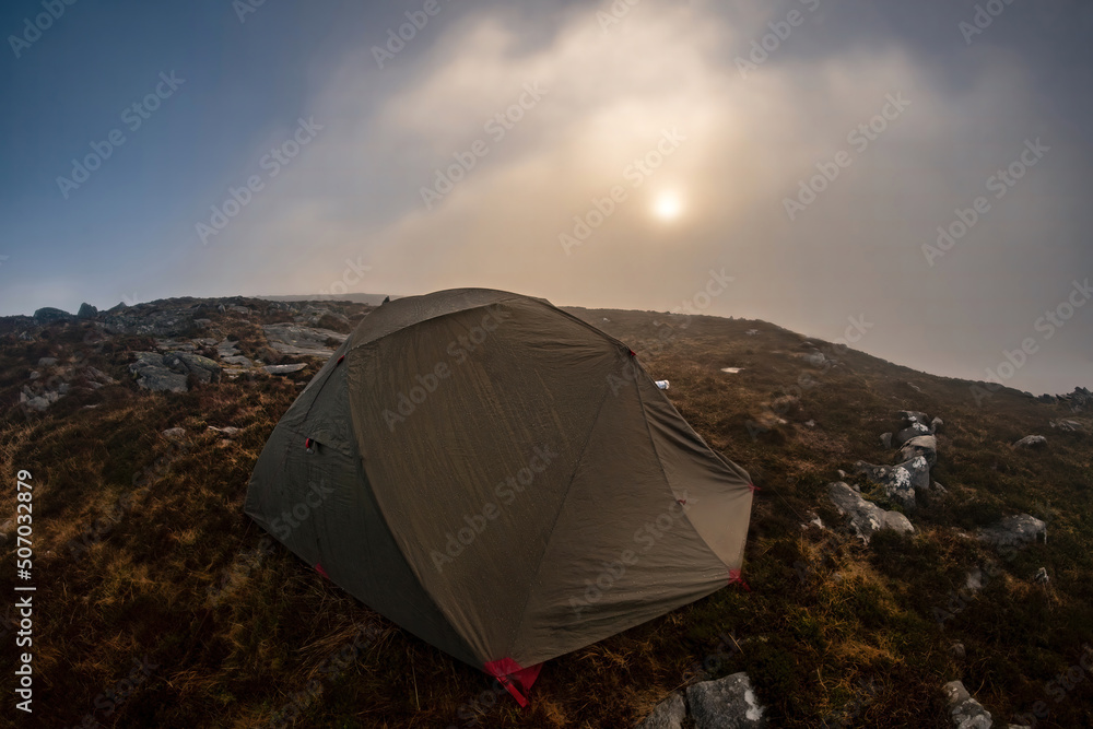 A wild camping tent in misty mountain weather 