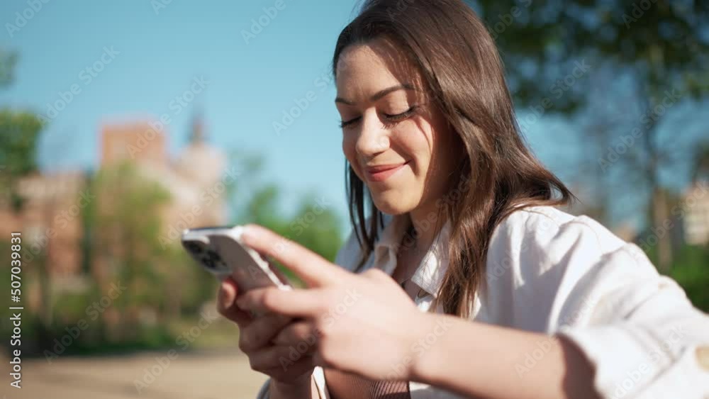 Laughing brunette woman typing on mobile while sitting on the bench Laughing brunette woman typing on mobile while sitting on the bench