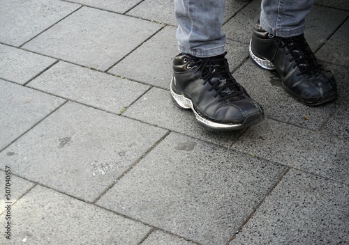 Schwarzes Paar Lederschuhe mit grauen Jeanshosenbeinen auf grauem Steinplatten in Stadt 