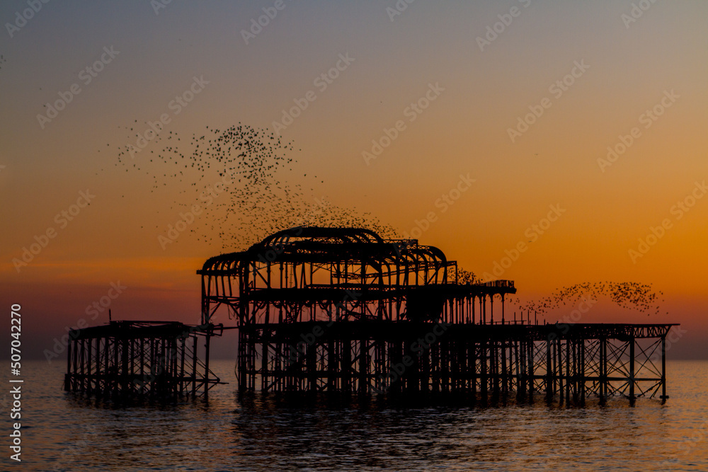Golden hour Brighton derelict West Pier at sunset with a starling murmuration 