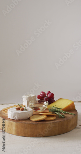 Vertical image of few types of cheese, biscuits and red grapes on wooden chopping board