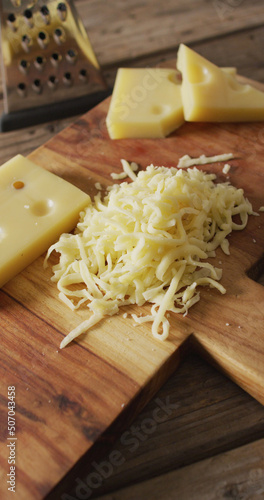 Vertical image of grated cheese and pieces of cheese with grater on wooden board