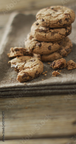 Vertical image of stack of chocolate chip cookies on cloth and wooden background
