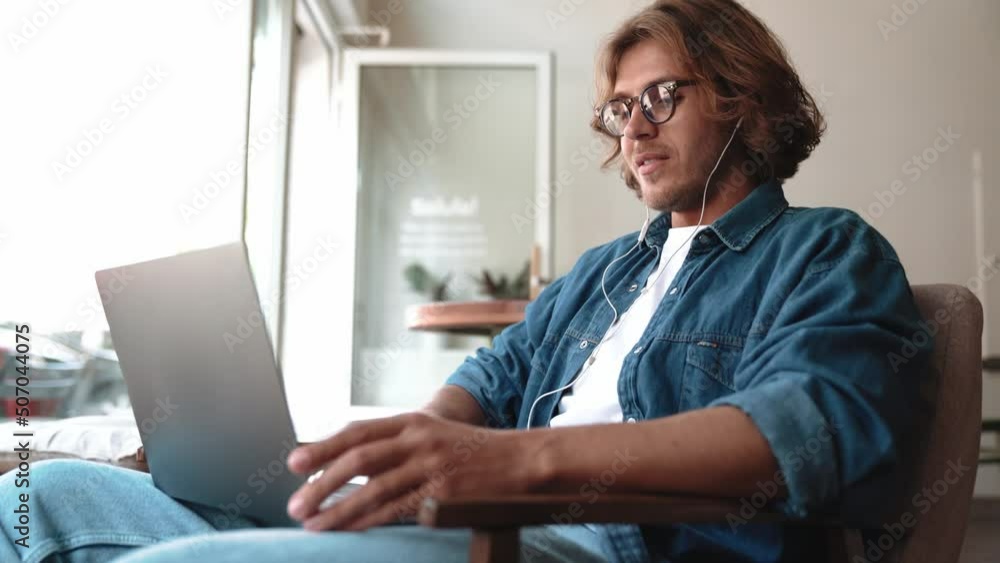 Positive blond man in eyeglasses talking by video call on laptop in cafe Positive blond man in eyeglasses talking by video call on laptop in cafe