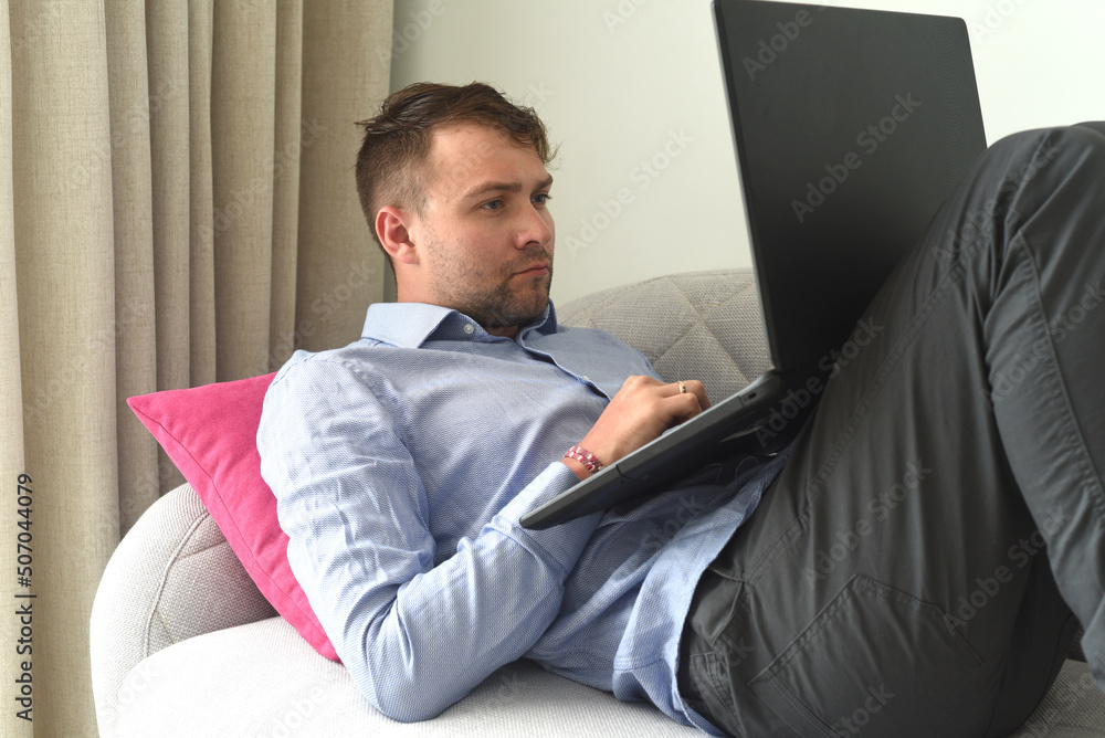 Young man freelancer working from home with his laptop laying on couch