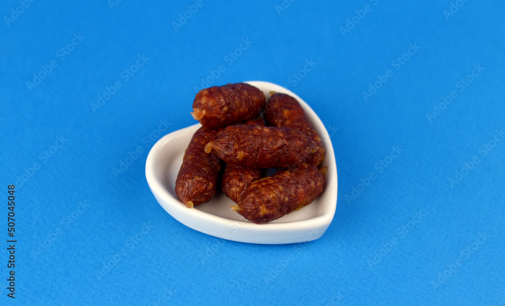 Small sausages in a white plate on a blue background Small sausages in a white plate on a blue background