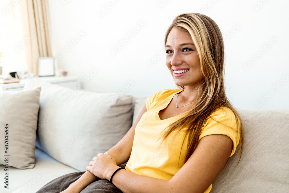 Portrait of a smiling young woman relaxing on the sofa at home. Cropped shot of attractive young woman wearing casual clothes while resting on sofa at home.