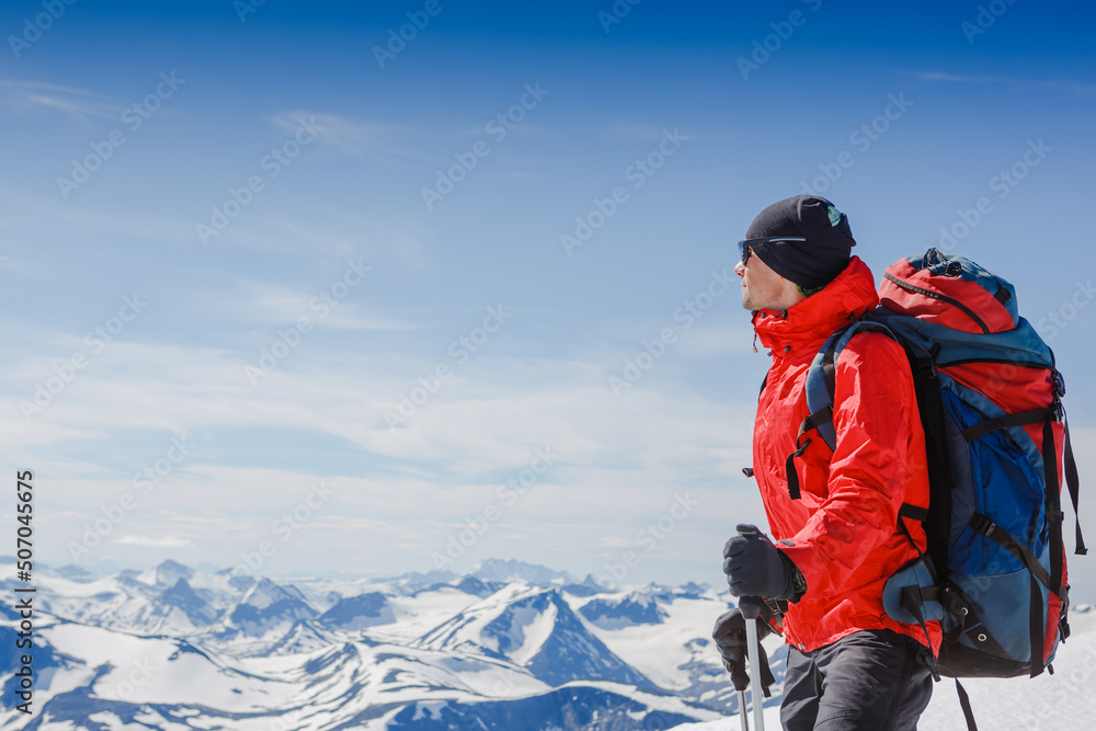 Hiker with backpack standing on top of a mountain and enjoying tne view