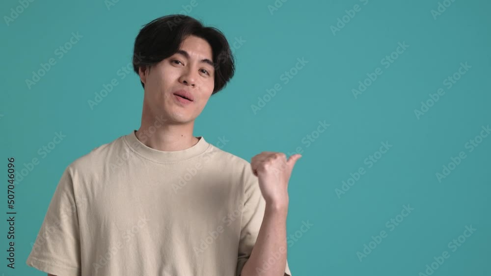 Smiling Asian brunet man pointing to the copy space in the blue studio Smiling Asian brunet man pointing to the copy space in the blue studio