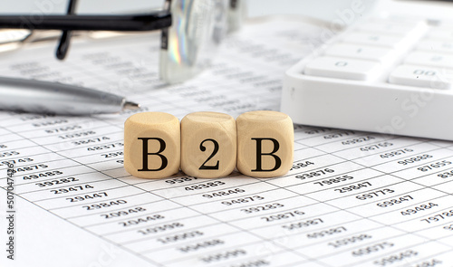 wooden cubes with the word B2B on a financial background with chart, calculator, pen and glasses, business concept.