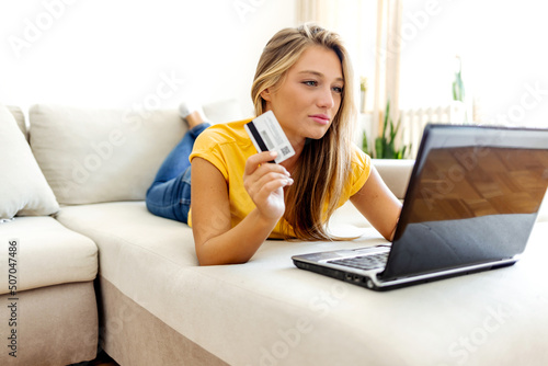 Shot of a young woman looking unhappy while using a laptop and credit card at home. Young woman sitting on her sofa and feeling confused while experience problem with her credit card.