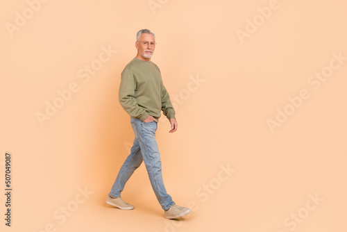 Full length photo of funky old grey hairdo man go wear eyewear pullover jeans sneakers isolated on beige background