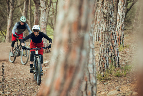Couple of enduro mtb riders, woman and man going down the mtb trail in the forest of Barcelona
