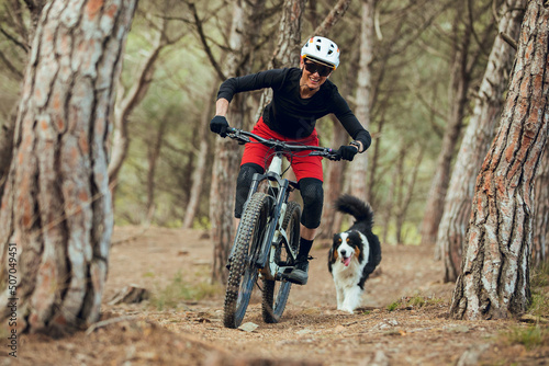Woman with mtb enduro bike going down mtb trail with her australian shepherd dog