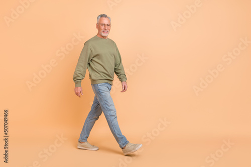 Full size photo of good elder grey hairdo man go wear eyewear pullover jeans footwear isolated on beige background