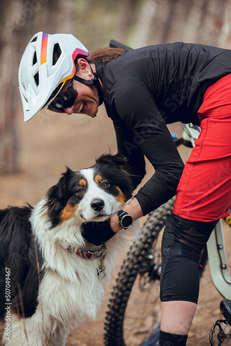 Girl with helmet and enduro mtb bike petting her australian shepherd dog in the mountains